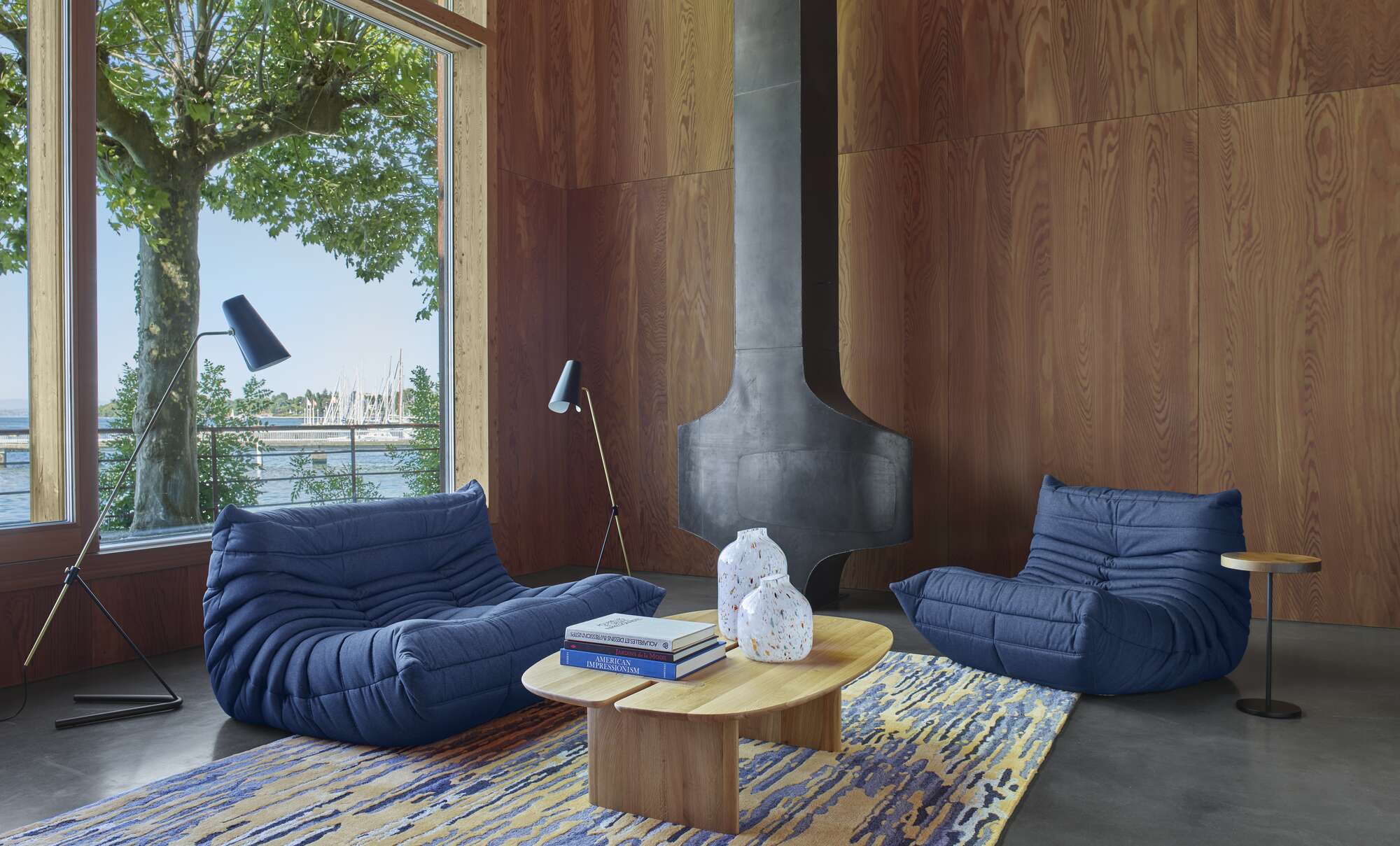 Modern living room with blue lounge chairs, a wooden coffee table, and a large window.